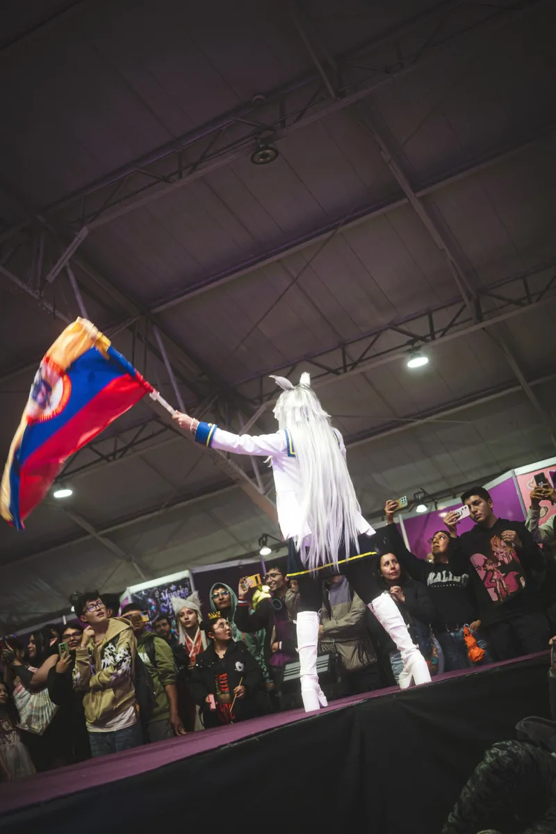 Cosplayer de Umamusume ondeando la bandera de Colombia frente al público en SOFA